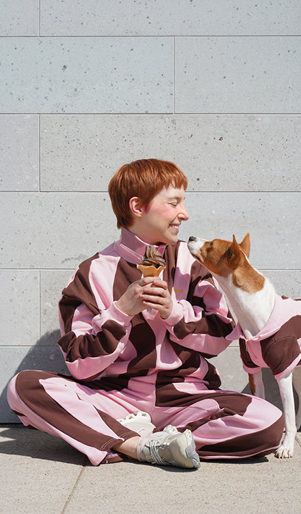 Woman and small dog in matching pink and brown wavy-stripe tracksuits sharing an ice cream cone — Sunbean matching dog and owner outfits